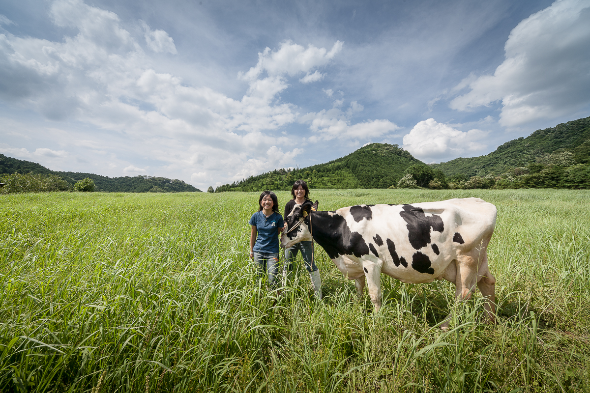 全国の生産地で出会った人々の記録、草原で牛と並ぶ生産者（姉妹） Record of people met at production sites across Japan, sisters standing with cows in a grassland